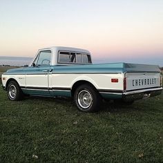 the truck is parked on the grass by the water in the evening hours and it's blue and white