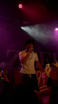 a man standing on top of a stage holding a microphone in his hand and wearing a white t - shirt