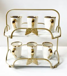 gold and white coffee cups are on a metal rack with two handles, one holding four mugs