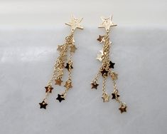 "more Gold dainty earrings in DearDanielleJewelry: https://www.etsy.com/shop/DearDanielleJewelry?ref=seller-platform-mcnav§ion_id=29399371 Shooting Star Earrings,Celestial Dangle Earrings. Star cascade, Star fall earring. Gold starry. Tiny sparkling little stars. 5/8\" diameter hammered gold plate star, 3\" drop Please choose your star color : Gold. Silver **framed gems, and charms in the jewelry is plated. *All the jewelry in my shop will be sent in cotton pouch. If you want gift box wrapping, Gold Star Dress, Fall Earring, Fun Necklaces, Star Earrings Dangle, Gold Star Earrings, Prom 2023, Starburst Earrings, Earrings Star, Cotton Pouch