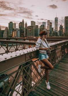 a woman standing on top of a bridge next to a cityscape with buildings in the background