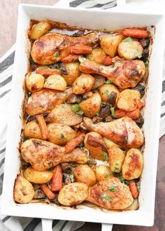 a casserole dish filled with chicken, potatoes and carrots on a striped cloth