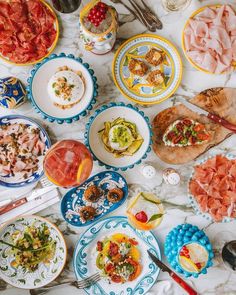 a table filled with plates and food on top of a white marble countertop next to utensils