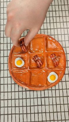 a person holding an egg and bacon shaped waffle on a plate with eggs in it