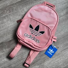 Adidas Originals Santiago Mini Backpack Nwt Pink/ Black Dimensions: 7.5" X 10" X 4.5". Adidas Originals Santiago Mini Backpack. Features Classic Adidas Trefoil Logo Screened On Front Zip Pocket With Contrasting Outline Along Front Pocket, Main Pocket, Back Panel, And Strap Adjusters. Zip Main Compartment With Small, Interior Sleeve. Large "Adidas" Script Screened Along Top Of Backpack. Adjustable Shoulder Straps. "The Brand With The 3 Stripes" Script Written In 3 Different Languages Screened On Everyday Pink Bags With Logo, Casual Pink Bag For Back To School, Pink Bag With Adjustable Strap For Back To School, Pink Bag With Zipper For Back To School, Pink Bag With Zipper Closure For Back To School, Sporty Pink Shoulder Bag For School, Casual Pink Shoulder Bag For Back To School, Trendy Logo Backpack Bag, Trendy Logo Backpack