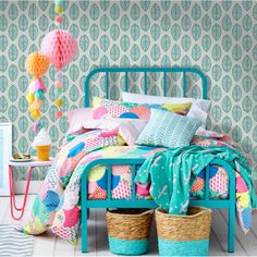 a room with a bed, basket and wallpaper on the walls is decorated in pastel colors