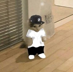 a teddy bear wearing a new york yankees hat and black shorts standing in front of a window