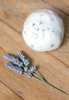 some lavender flowers are sitting on a wooden surface next to a ball of soap that is white