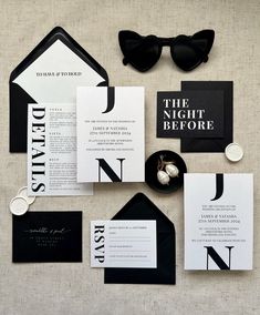 an assortment of black and white wedding stationery with sunglasses on the top, including lettered envelopes