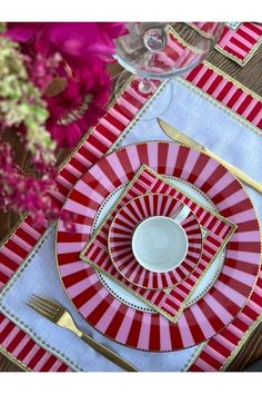 the table is set with red and white plates, silverware, and pink flowers