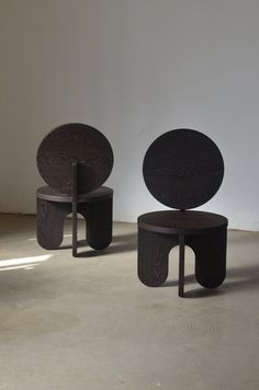 two wooden stools sitting next to each other on top of a cement floor in front of a white wall