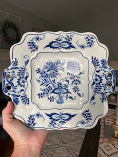 a hand holding a blue and white plate with flowers on it in front of a table