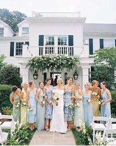 a group of women standing next to each other in front of a white house with flowers