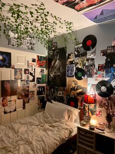 an unmade bed in a dorm room with records on the wall and plants hanging from the ceiling