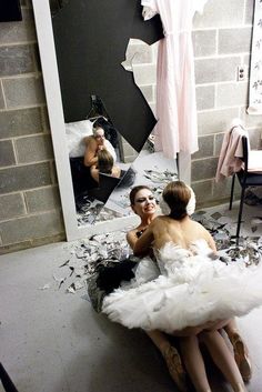 two women sitting in front of a mirror with shattered glass on the floor and walls