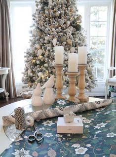 a christmas tree in the corner of a living room with candles and ornaments on the table