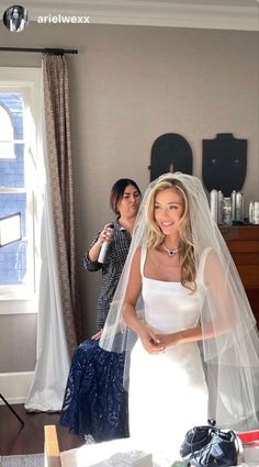 a woman in a wedding dress standing next to another woman wearing a veil and holding a bottle