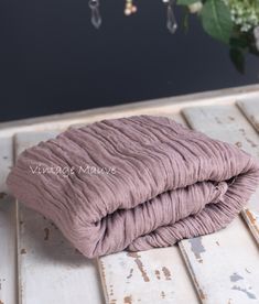 two pink blankets sitting on top of a wooden table next to a vase with flowers