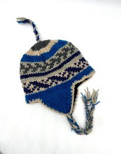 a blue and gray knitted hat with two tassels on the brim