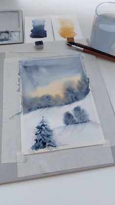 some watercolors are sitting on a table and there is a painting in the background