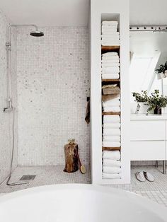 a bathroom with white tiles and towels on the shelf next to the bathtub is shown