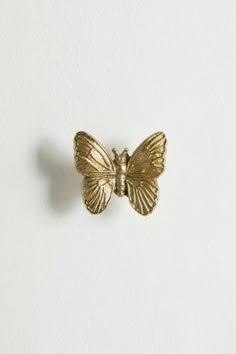 a gold butterfly pin sitting on top of a white wall