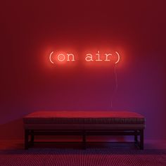 a red neon sign that says on air above a bench in front of a pink wall