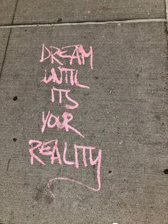 graffiti written on the sidewalk says dream until it's your reality with pink spray paint