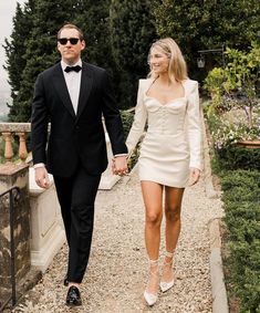 a man in a tuxedo and a woman in a white dress walking down a path