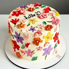 a white cake decorated with colorful flowers and the word hello spelled on it's side