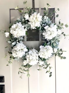 a wreath with white flowers and greenery hangs on a door