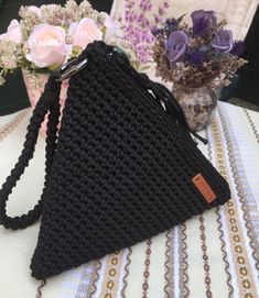 a black crocheted purse sitting on top of a table next to some flowers