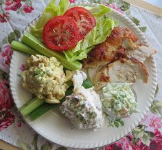 a white plate topped with lots of food on top of a floral covered table cloth