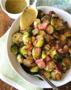 a white bowl filled with brussel sprouts and bacon next to a spoon