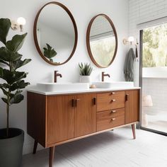 two round mirrors are above the double sinks in this modern bathroom with wood cabinetry and white tile flooring