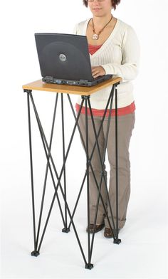 a woman using a laptop computer on top of a wooden table with black metal legs