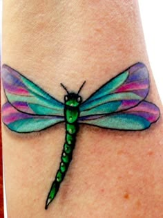 a colorful dragonfly tattoo on the wrist is shown in green and pink colors,