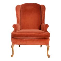 an orange velvet wingback chair with wooden legs