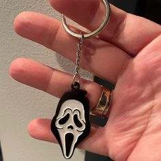 a hand holding a black and white keychain with a ghost face on it