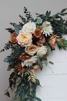 an arrangement of flowers and greenery against a white wall