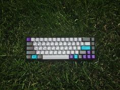 a keyboard sitting in the grass on top of it's side with blue and purple keys