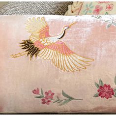 a pink pillow with an embroidered crane on it's side and flowers in the background