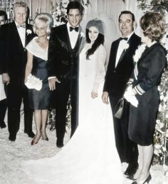 a group of people standing next to each other in front of a wedding arch with flowers on it