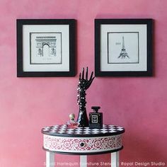 two framed pictures hang on the wall above a small table with an ornate black and white design