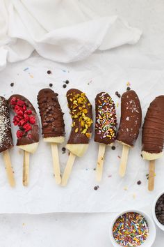 five chocolate covered ice cream pops are lined up on a paper towel with sprinkles