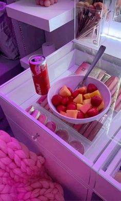 a bowl of fruit is on display in a pink case next to a can of soda