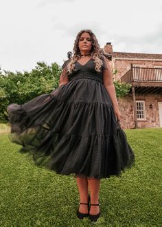 a woman standing in the grass wearing a black dress