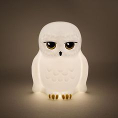 a white owl sitting on top of a table next to a light bulb with yellow eyes