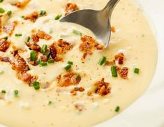 a white bowl filled with soup topped with bacon and green onions next to a spoon