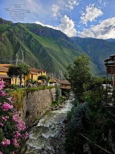 a river running through a lush green hillside covered in flowers and surrounded by tall mountains